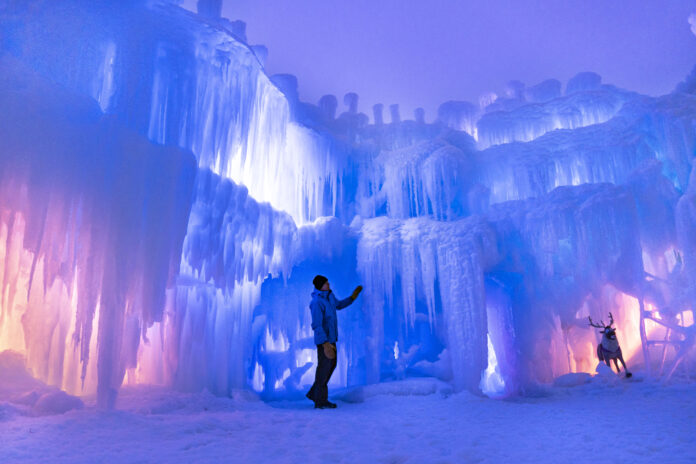 A glowing ice palace at night with vibrant blue and purple LED lights illuminating crystalline ice tunnels.