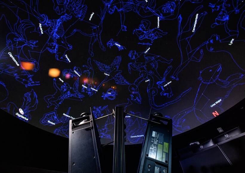 A dark domed ceiling of a planetarium displaying a brilliant map of constellations and stars.