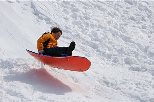 Rolling sand dunes covered in white snow with a person sledding down a steep slope at sunset.