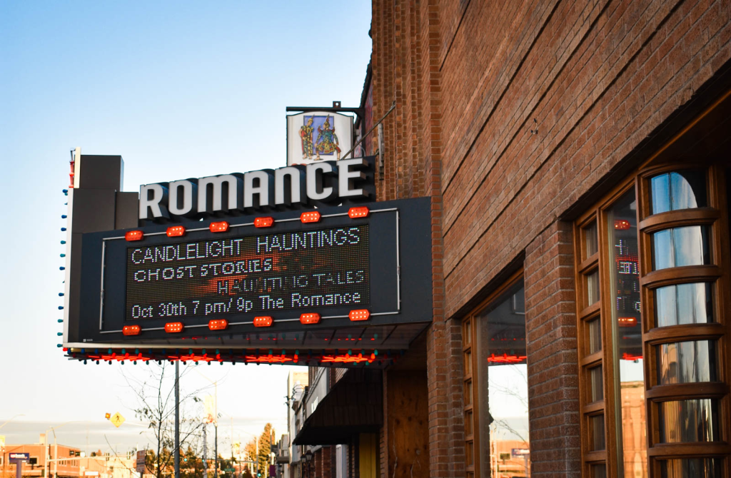 The vintage neon marquee of The Romance Theater in Rexburg lighting up a snowy downtown street at dusk.