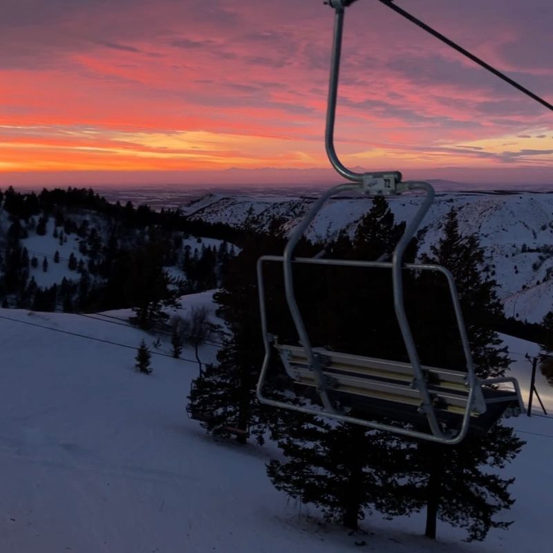 A wide shot of ski slopes at night under bright floodlights with skiers gliding down the mountain.